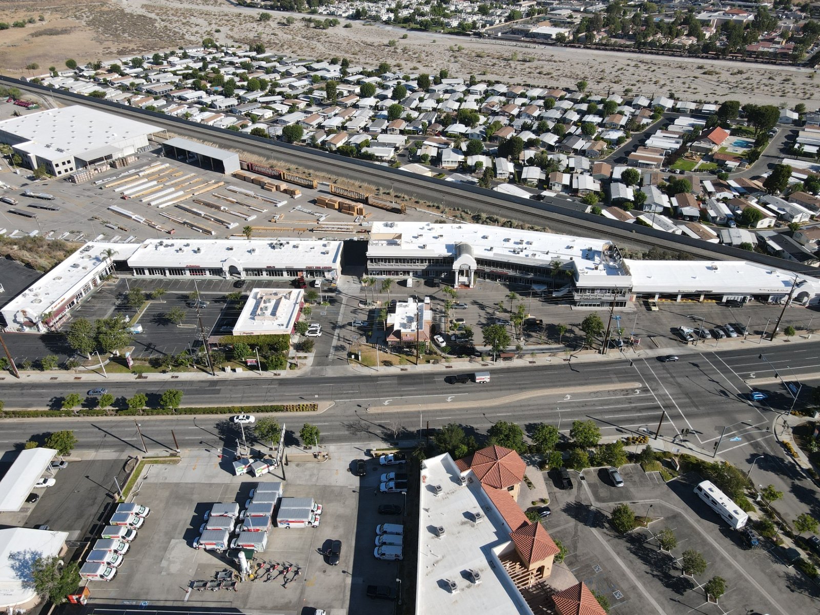 Aerial view of a commercial retail center and surrounding buildings with restored white reflective roofs