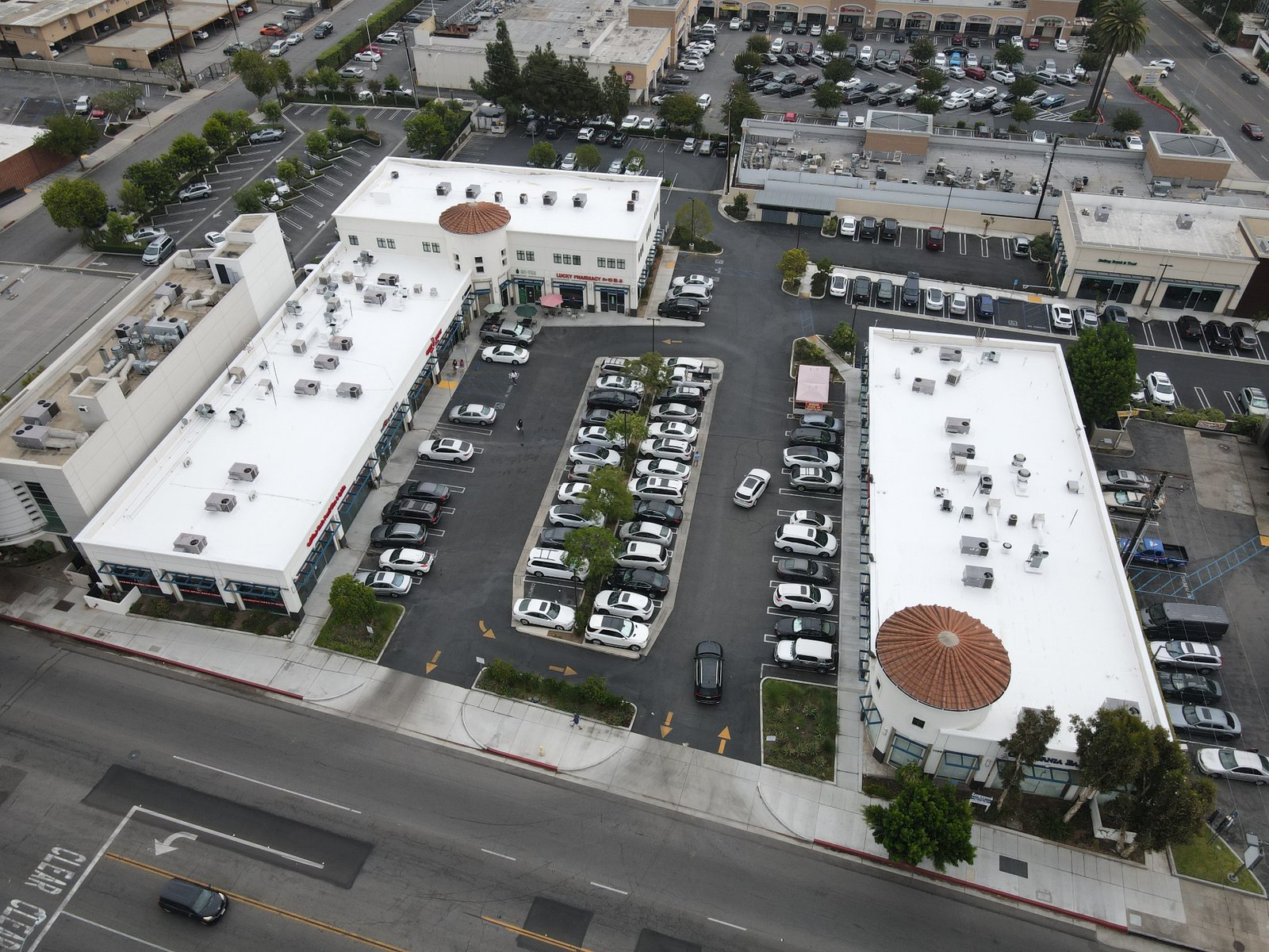 Aerial view of a shopping center with multiple buildings featuring restored white reflective roofs
