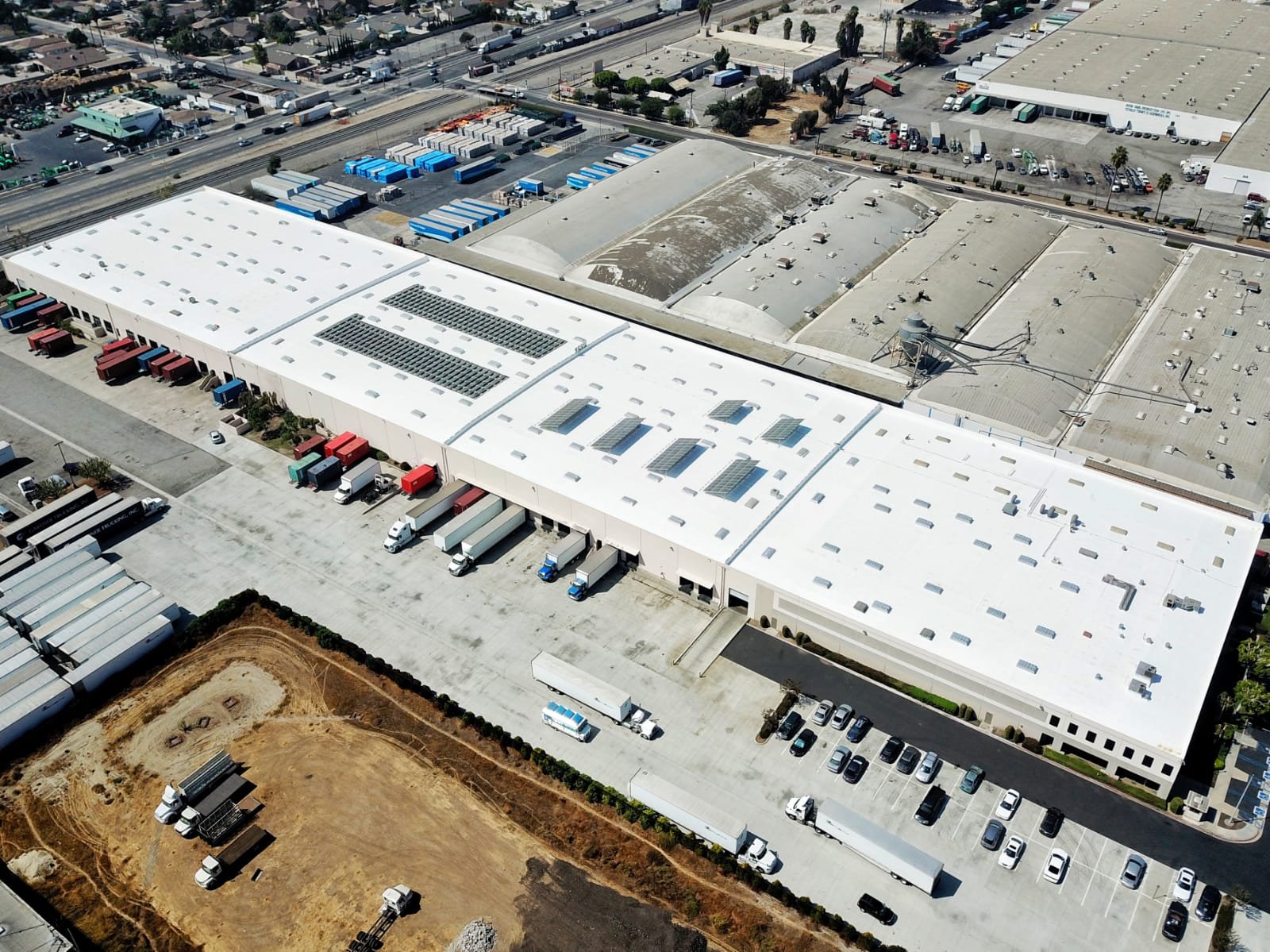 Aerial view of a large commercial warehouse with a restored white reflective roof and solar panels